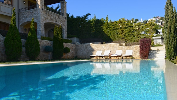 En pool med kristallklart vatten, solstolar och en arkitektur som präglas av sten.