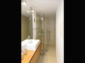Une salle de bain moderne avec une douche à l’italienne en verre, un lavabo blanc et un miroir au-dessus du meuble-lavabo.