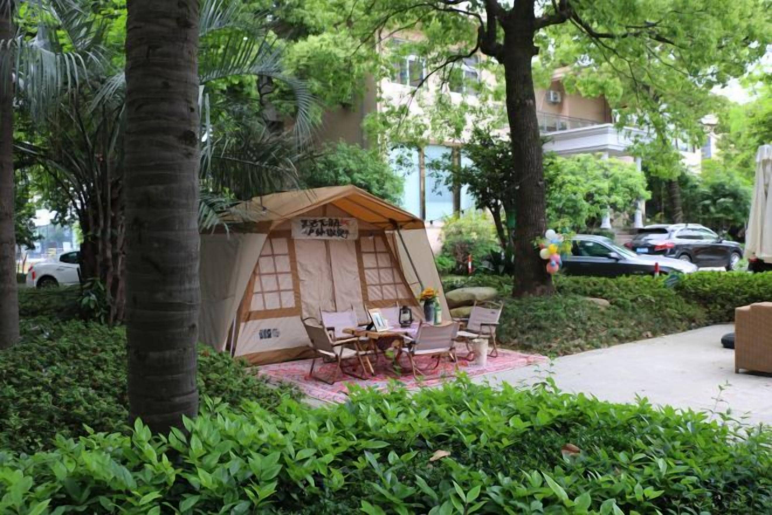 A small, enclosed outdoor seating area with a table and chairs, surrounded by lush greenery and trees.