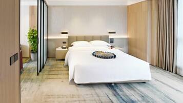 A modern hotel room with a large bed, bedside tables, a nightstand, a potted plant, and a view of the city.