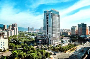 Un edificio moderno de gran altura, rodeado de vegetación y otros edificios.