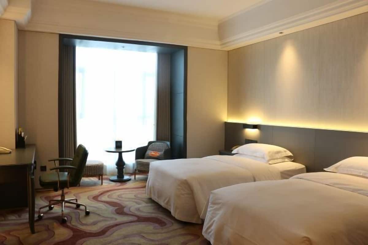 Camera d'albergo con due letti, una scrivania, una sedia e un piccolo tavolo.