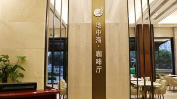 A reception area with a reception desk, a vertical sign with text, and a view of the dining area with tables and chairs.