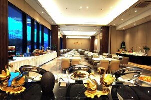 Un salón de banquetes con mesas dispuestas para comer, un bufé con diversas opciones de comida y un gran ventanal con vistas al exterior.