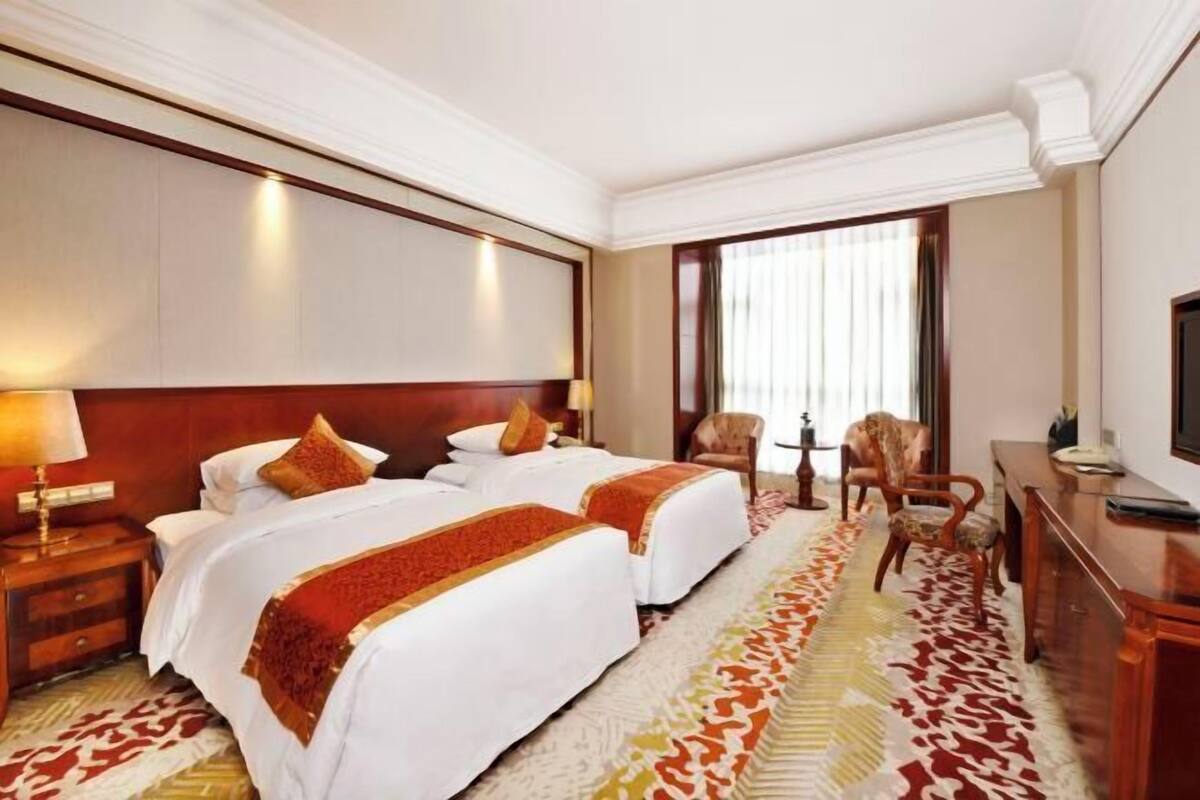 Una camera d'albergo con due letti, una scrivania, una sedia e un'ampia finestra.