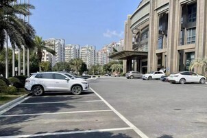 Un estacionamiento con varios coches, un edificio con acceso cubierto y edificios residenciales altos al fondo.
