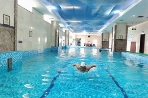 Piscina interior con marcas claras de carriles, piso de baldosas y techo con diseño de nubes.