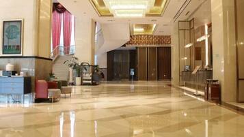 A spacious lobby with a check-in counter, seating area, and a staircase leading to upper floors.