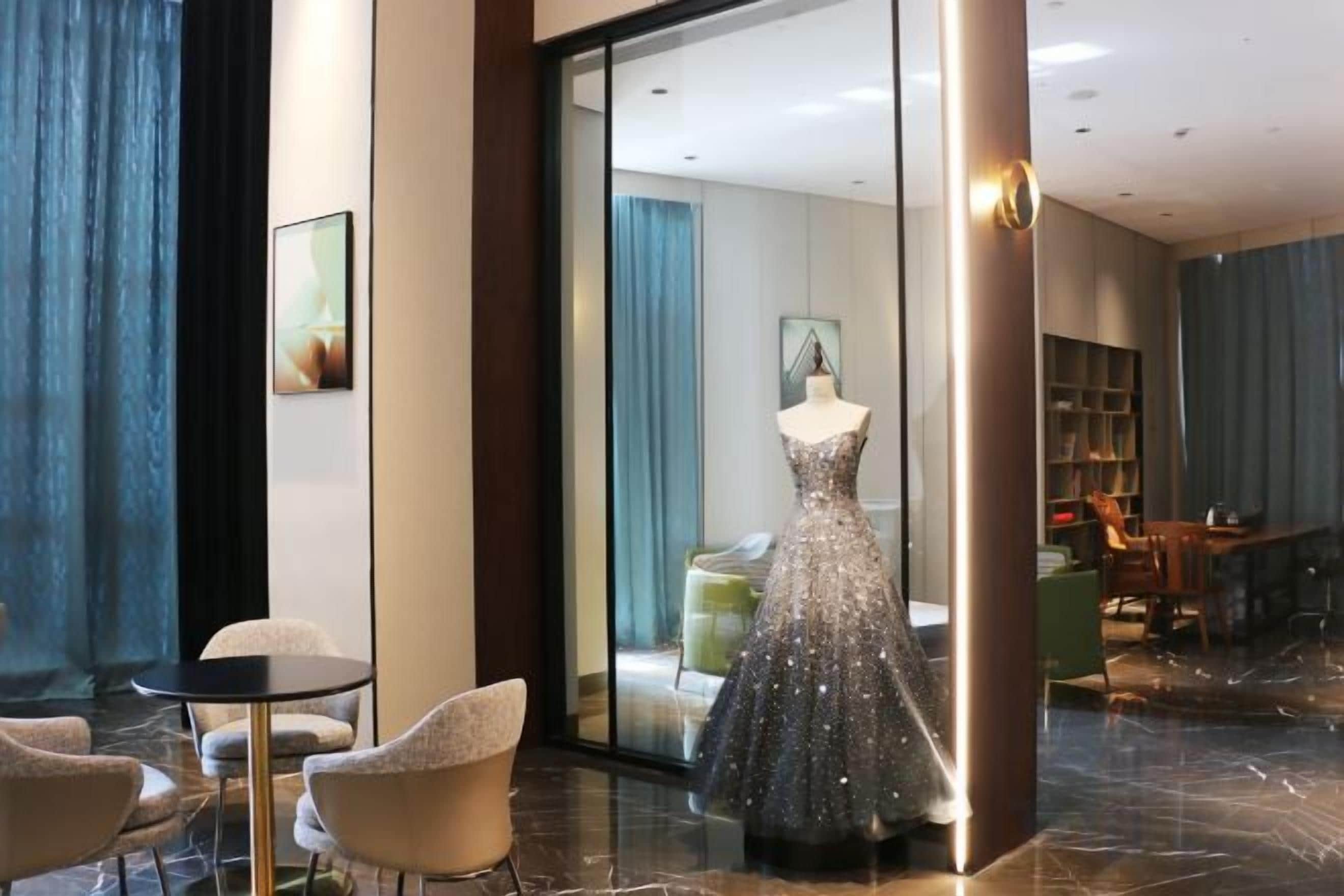 A hotel lobby with a mannequin in a dress, a seating area, and a view into a room.