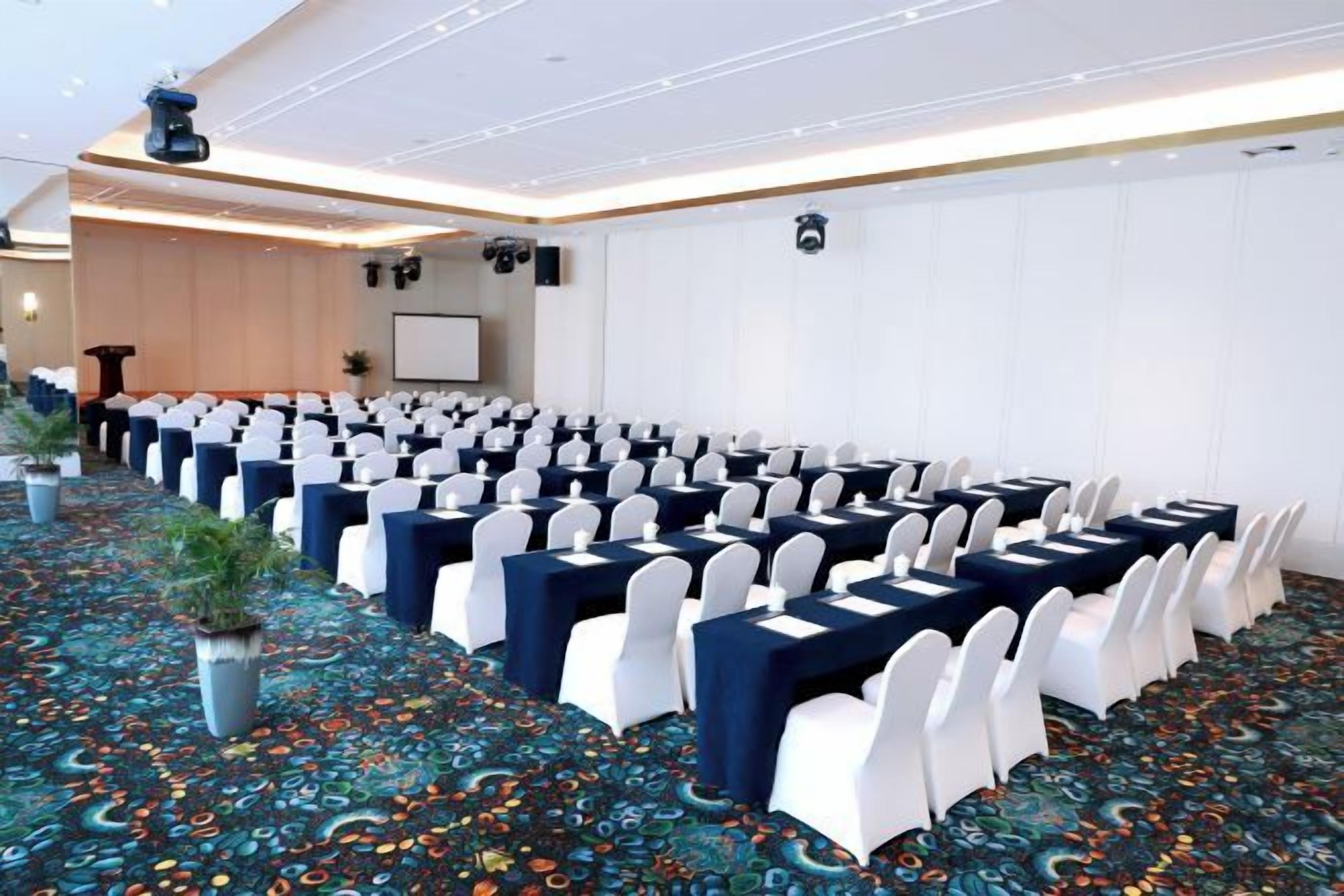Una sala conferenze con file di tavoli e sedie, pavimento con moquette e una lavagna a parete.