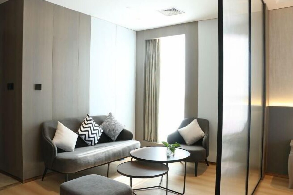 A modern room with a grey sofa, two armchairs, a small round table, and a large window with curtains.