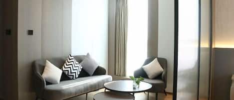 A modern room with a grey sofa, two armchairs, a small round table, and a large window with curtains.