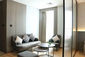 Una habitación moderna con un sofá gris, dos sillones, una mesita redonda y un ventanal con cortinas.
