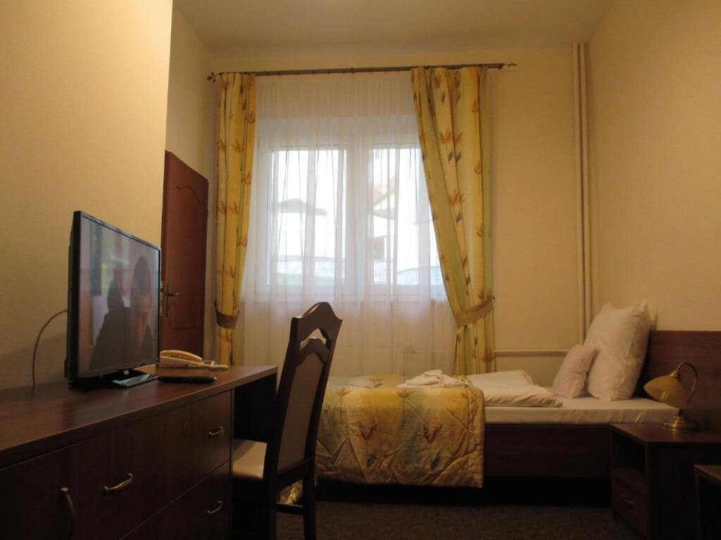 A bedroom with a bed, a desk with a television, and a chair.