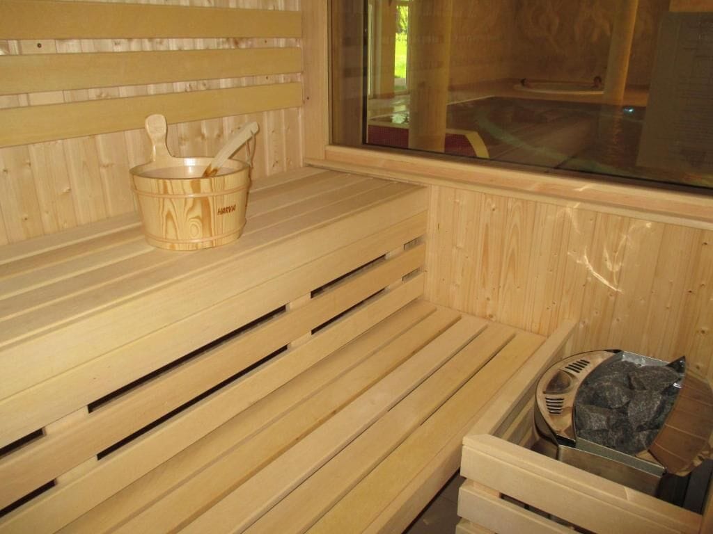 A wooden sauna with benches, a wooden bucket with a ladle, and a stone-filled container.