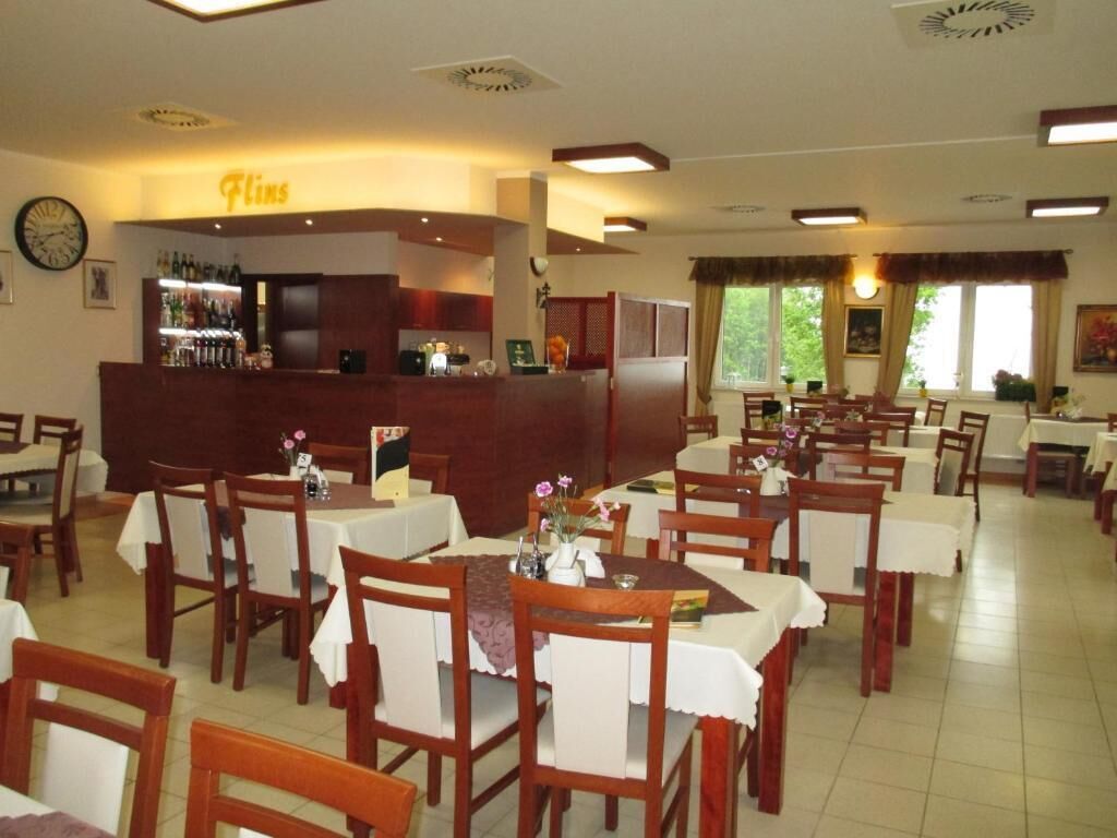 A restaurant with multiple tables and chairs, a bar area, and a clock on the wall.