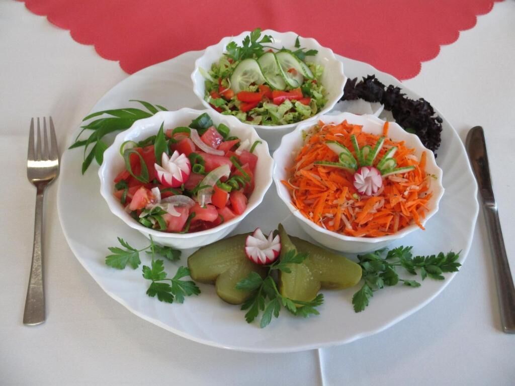 Une assiette avec trois bols de salade, une fourchette et un couteau, le tout posé sur une table recouverte d’une nappe rouge.