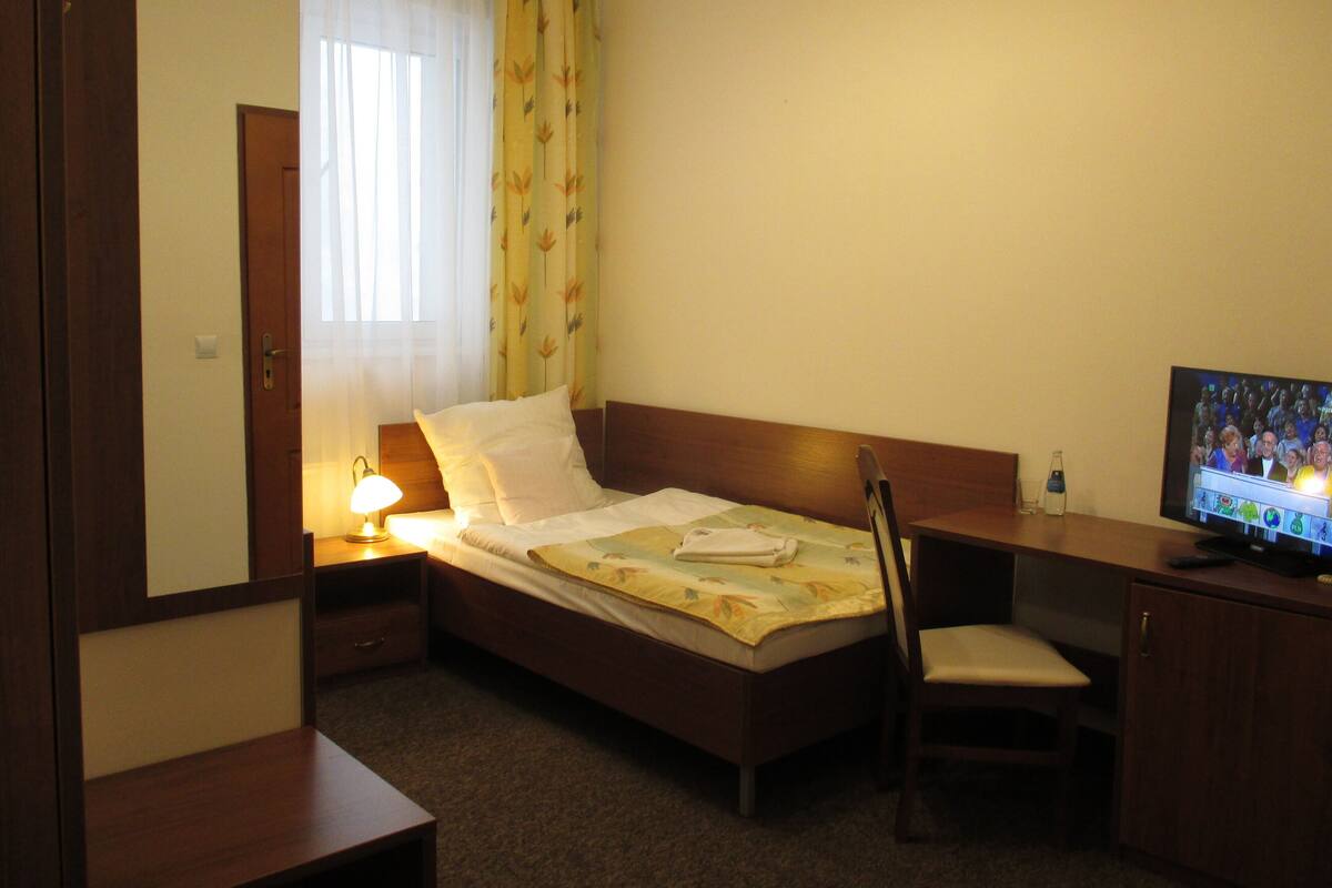 Hotelkamer met een bed, een bureau, een stoel, een televisie en een raam met gordijnen.