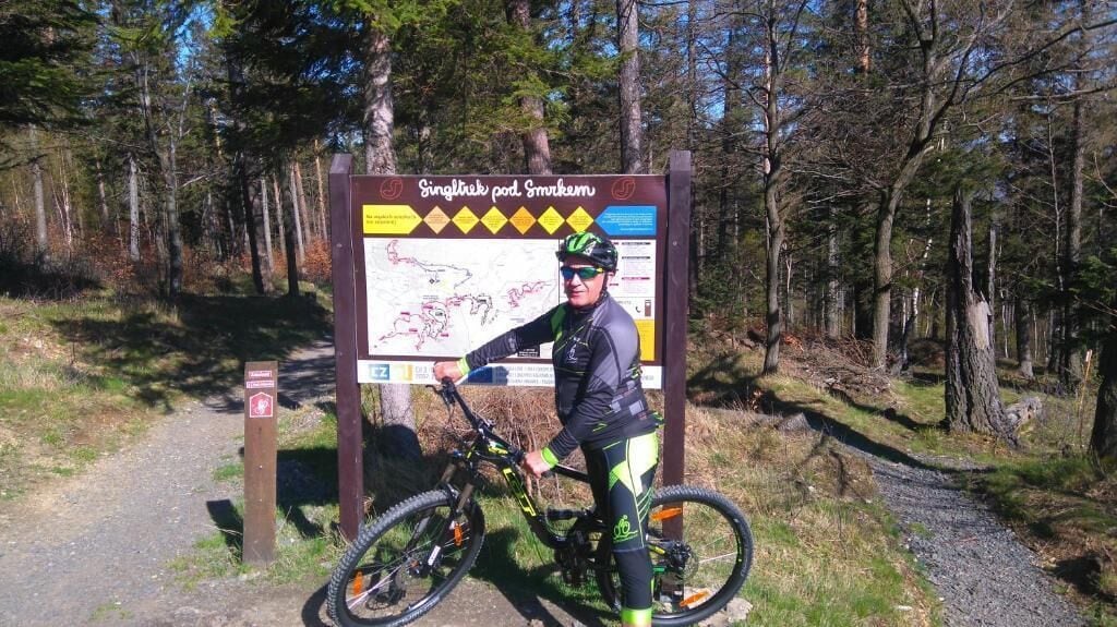 Un cartel con un mapa y texto, una persona en bicicleta y una zona boscosa.