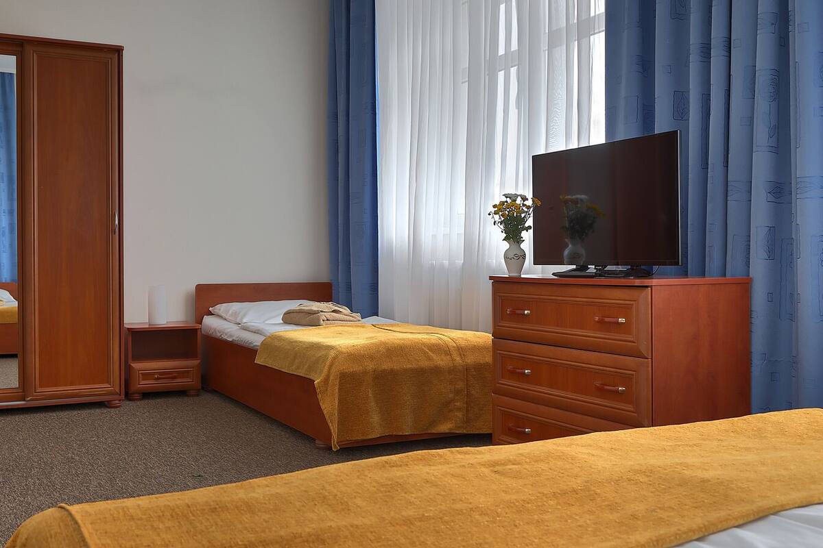 Een hotelkamer met een enkel bed, een houten dressoir, een televisie en een spiegel.