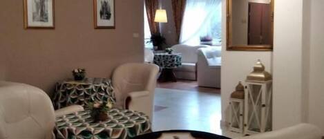 Una sala de estar con un sofá, sillones, una mesita con estampado y un cartel enmarcado.