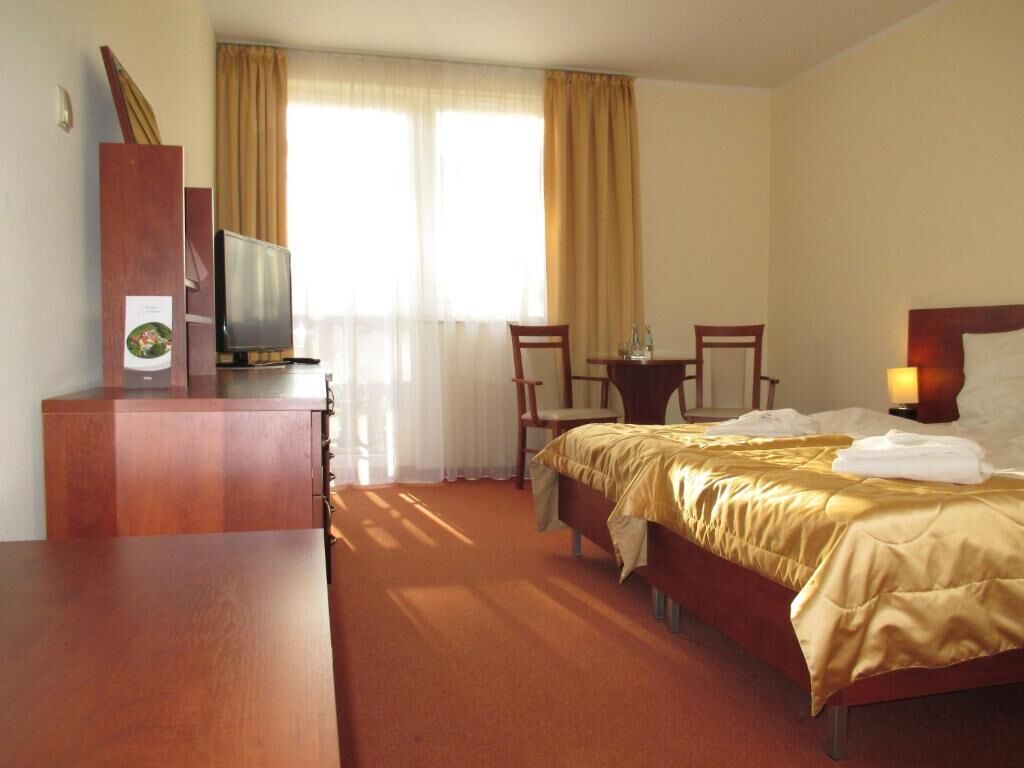 Habitación de hotel con cama, escritorio, silla, televisor y ventana con cortinas.