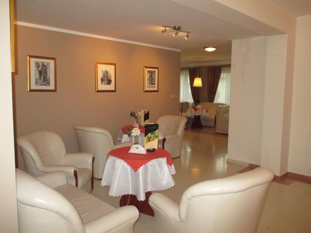 A hotel room with a dining area featuring a table with a red tablecloth, white chairs, and framed artwork on the walls.