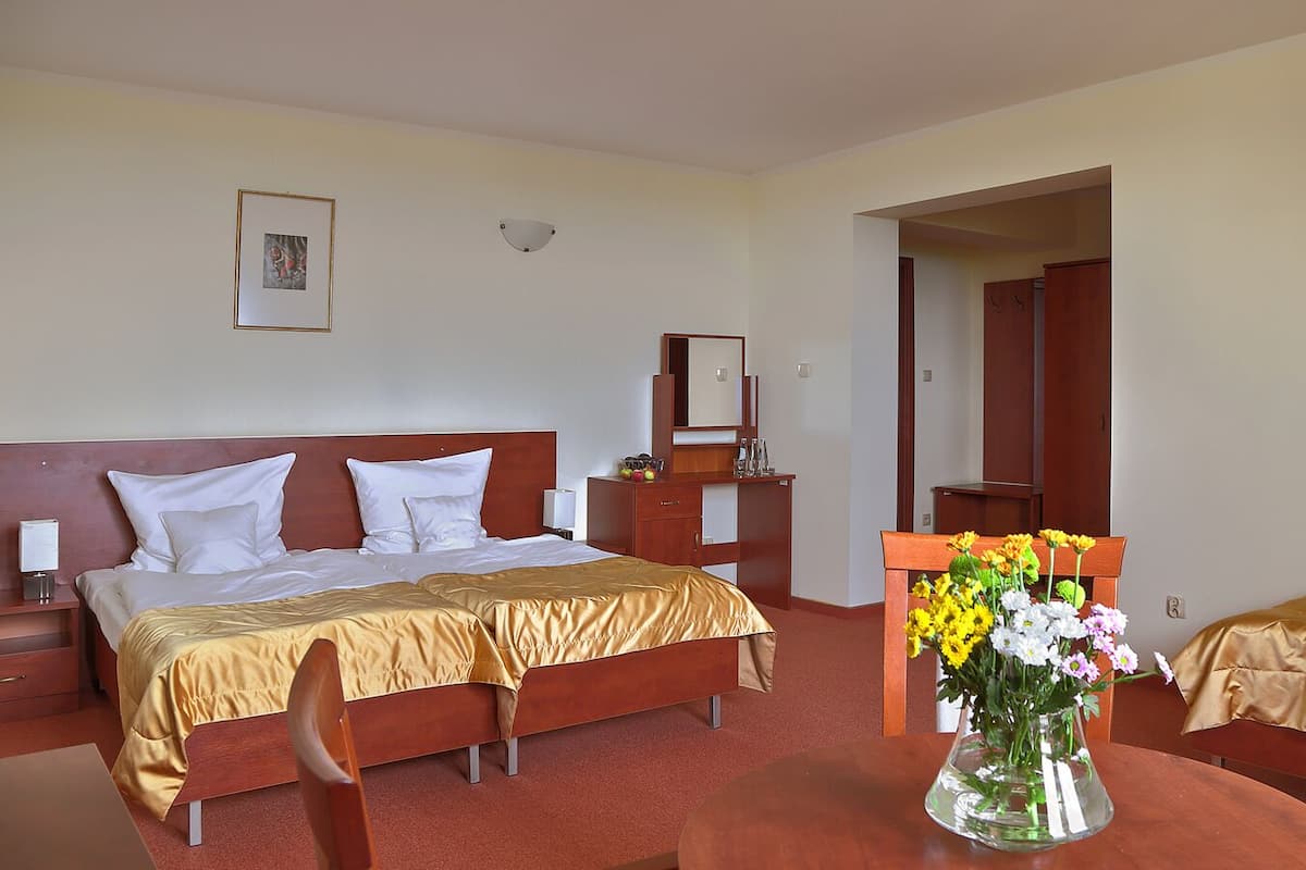 Een hotelkamer met een tweepersoonsbed, een eenpersoonsbed, een nachtkastje, een dressoir, een spiegel en een vaas met bloemen.