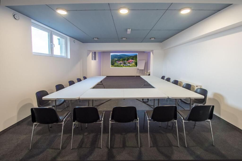 A conference room with a long table, black chairs, a projector screen, and a view of a landscape through a window.