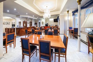 A spacious dining area with multiple wooden tables and chairs, a chandelier, and a television mounted on the wall. - Hotel am Bayrischen Platz (Leipzig)