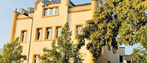 A hotel building with a prominent "Hotel" sign on the facade, multiple windows, and a tree in the foreground.