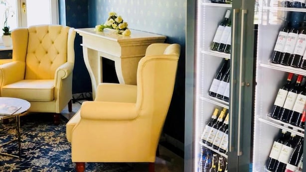 Una stanza con due poltrone gialle, un tavolino con un vaso e un frigorifero per vino pieno di bottiglie.