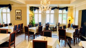 Zona pranzo con diversi tavoli e sedie, un lampadario e ampie finestre con tende.