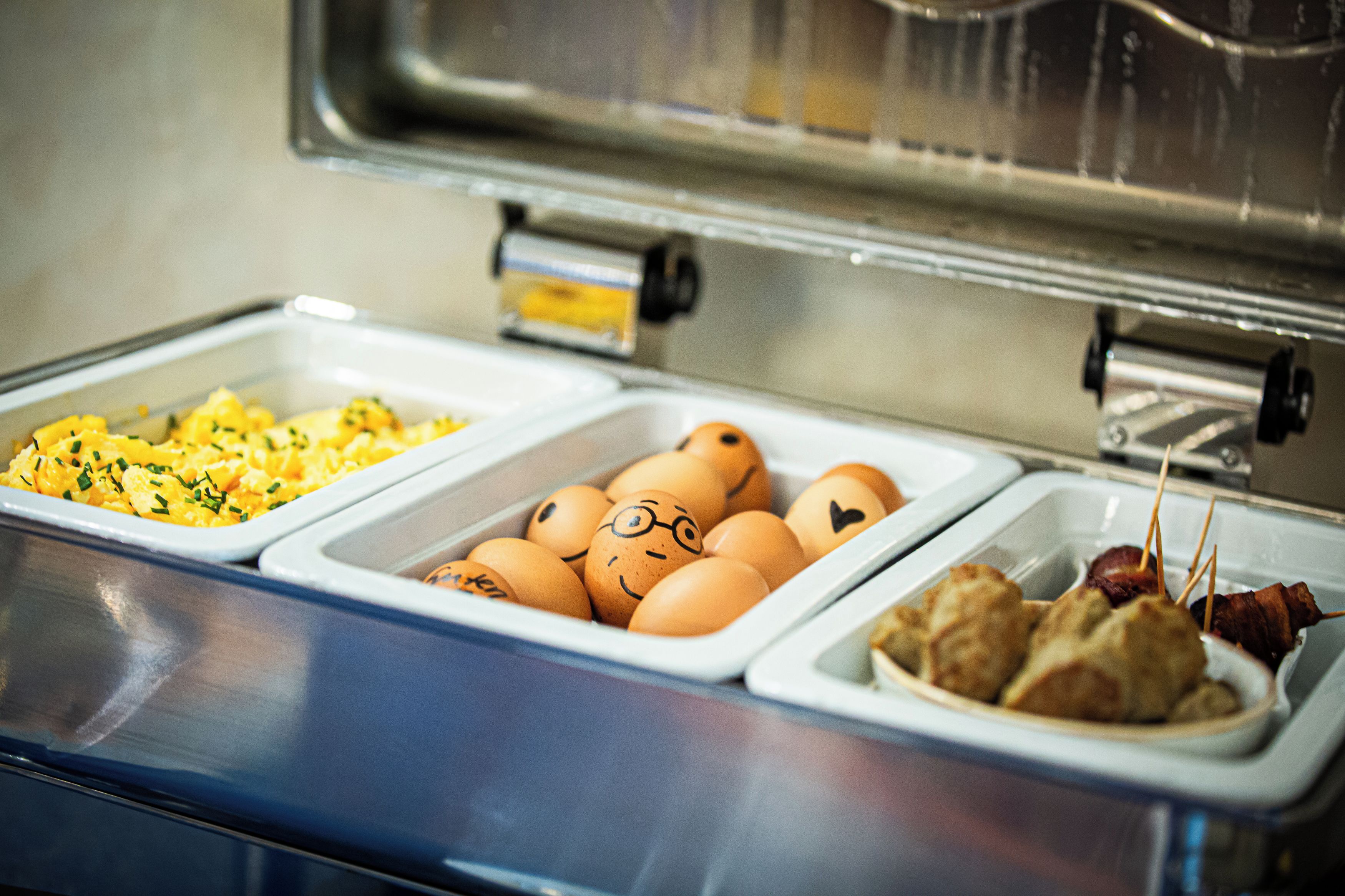 A buffet with scrambled eggs, decorated eggs, and bacon-wrapped meat skewers.