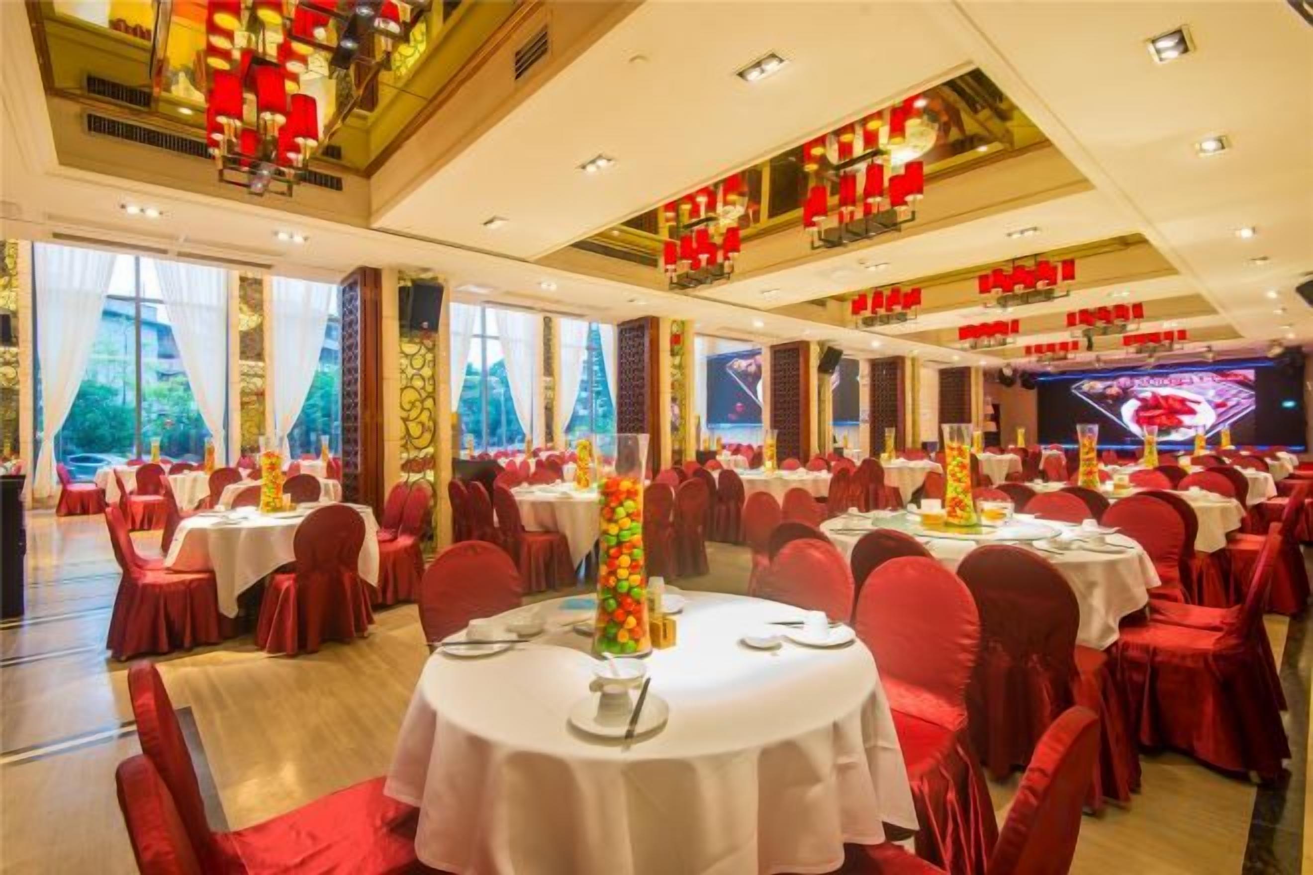 A banquet hall with round tables, red chairs, and a stage with red decorations.