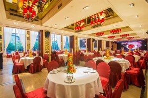 A banquet hall with round tables, red chairs, and a stage with red decorations. - Hejiang Peninsula Hotel (Fengkai)