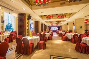 A banquet hall with round tables, red chairs, and a stage at the far end.