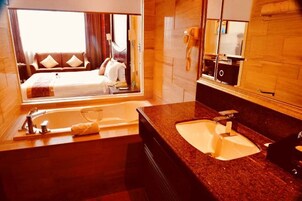 A hotel room with a large bed, a bathroom with a sink and mirror, and a view of the room through a window.