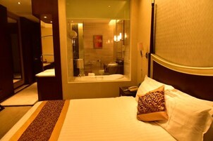 A hotel room with a large bed, a bathroom with a glass shower enclosure, and a bedside table with a lamp.