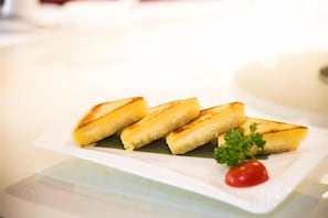 A white rectangular plate with grilled breadsticks and a small red cherry tomato on a reflective surface. - Hejiang Peninsula Hotel (Fengkai)