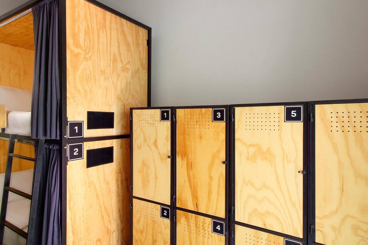 A set of wooden lockers with numbered compartments, a bunk bed, and a small desk with a lamp.