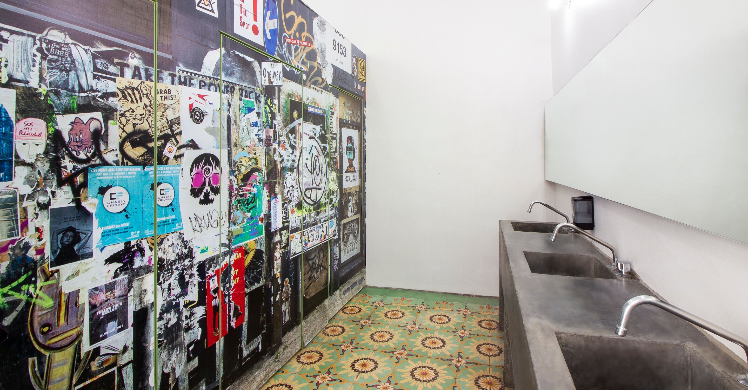 Een badkamer met een wastafel en een muur vol stickers en posters.