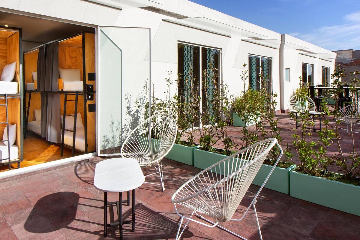 A modern hotel room with a balcony, a white sofa, and two white chairs.