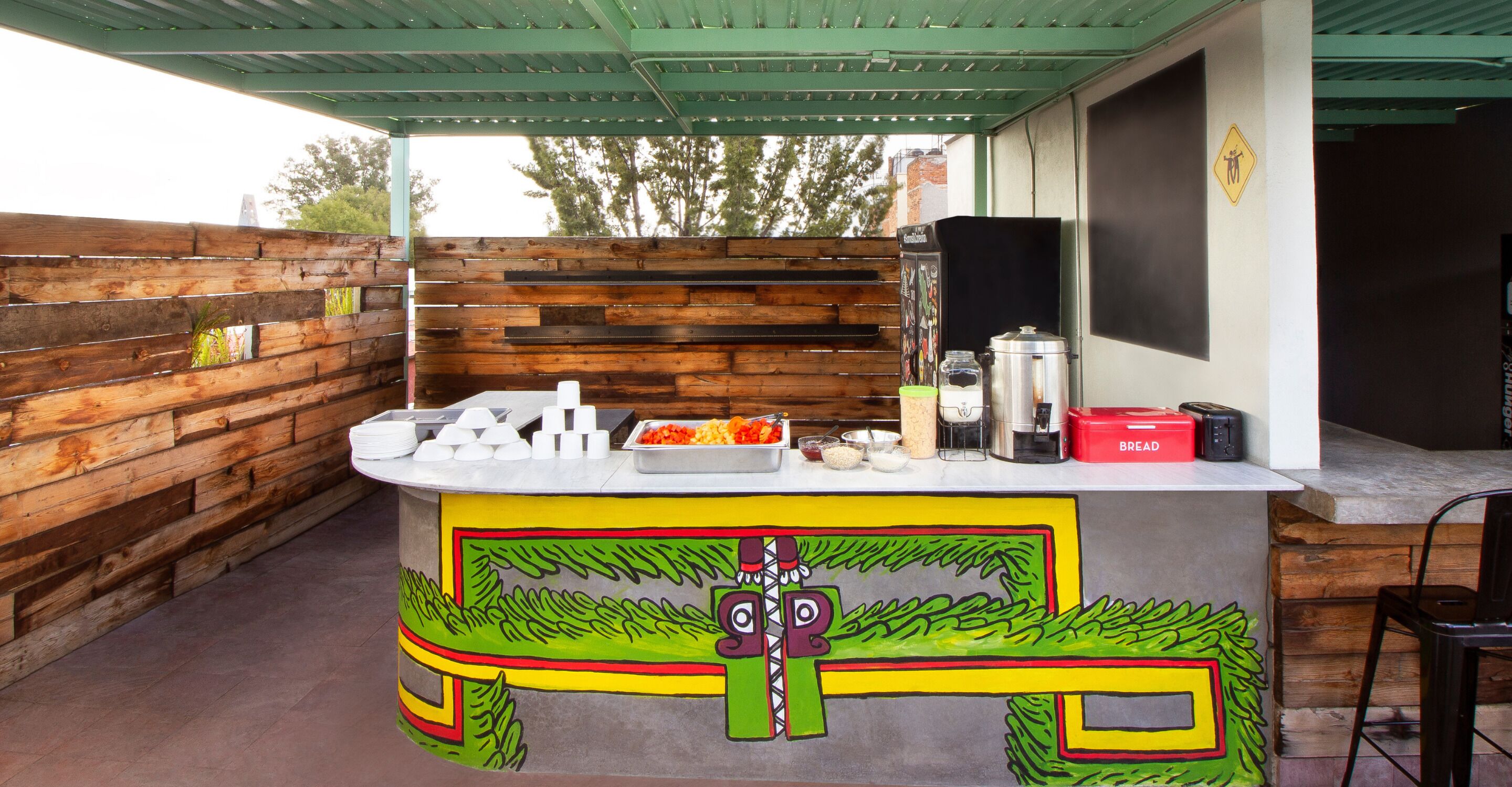 Eine Bar mit Holzbeschreibung, einer Theke mit Speisen, einer Kaffeemaschine und einer Brokkiste.