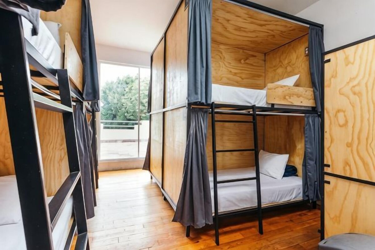 A bunk bed room with a wooden floor, a window, and a curtain.