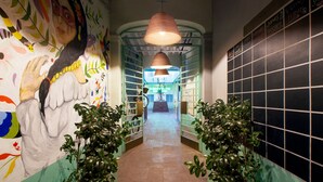 Un pasillo con un mural, estanterías verdes y una pared de azulejos negros con un calendario.