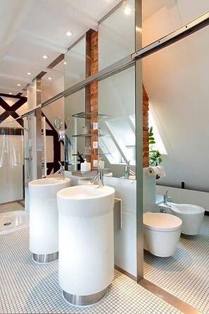 Un baño moderno con dos lavamanos grandes, una ducha y un área de inodoro con cerramiento de vidrio.