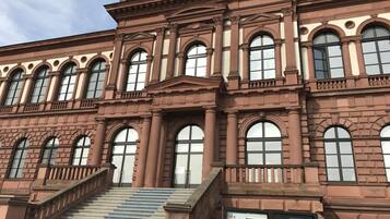 Un edificio grande e histórico con varias ventanas arqueadas y una escalera monumental que lleva a la entrada.