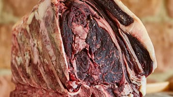 A large, raw beef cut with visible marbling and fat layers, placed on a wooden surface.