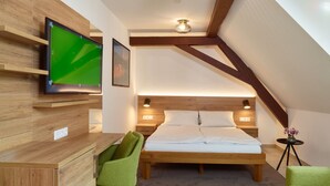 Een moderne slaapkamer met een houten bureau, een groene stoel, een bed met witte lakens en een aan de muur bevestigde televisie.